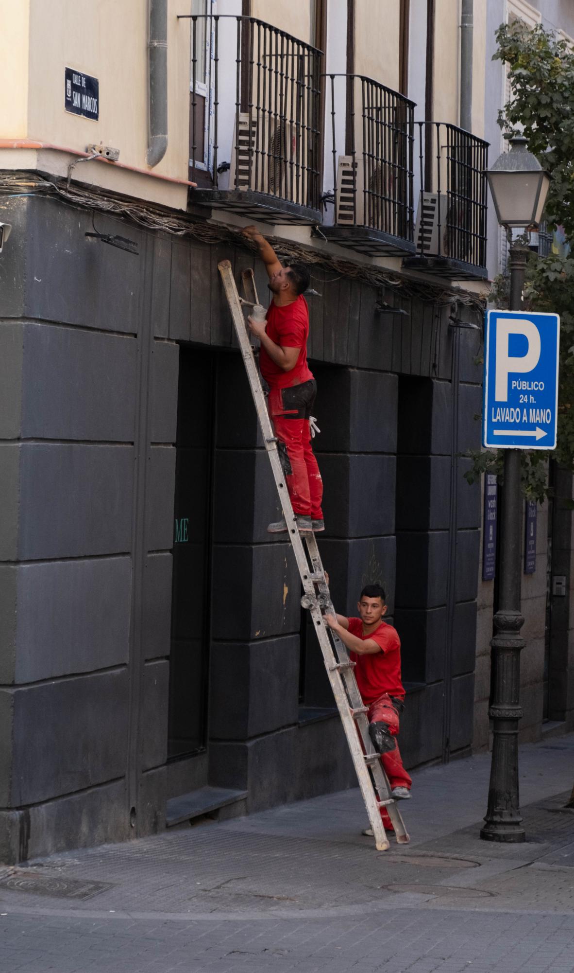 Two men paint a building in Chueca, Madrid.