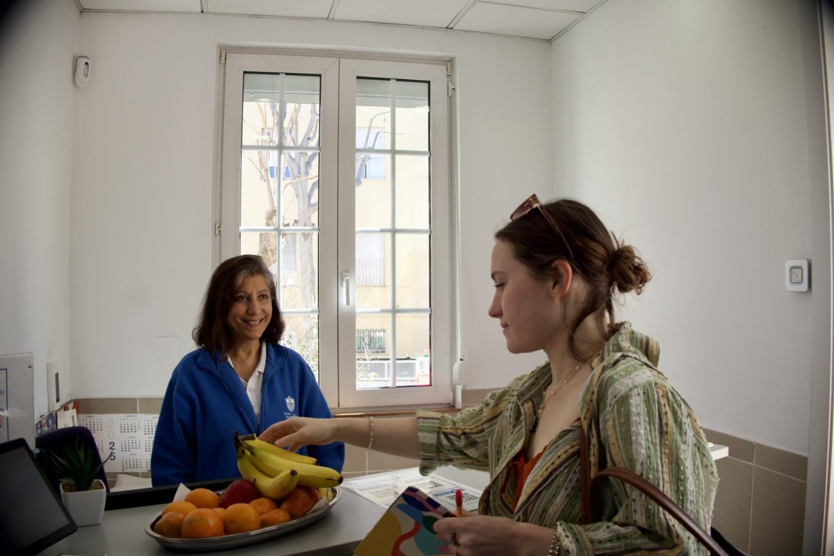 Beloved receptionist Roweena Sehwani smiles to welcome a student entering PRH. The student reaches toward a bowl of fruit set out each day during the month of Ramadan by the Campus Ministry as a break-the-fast snack for the Muslim community.