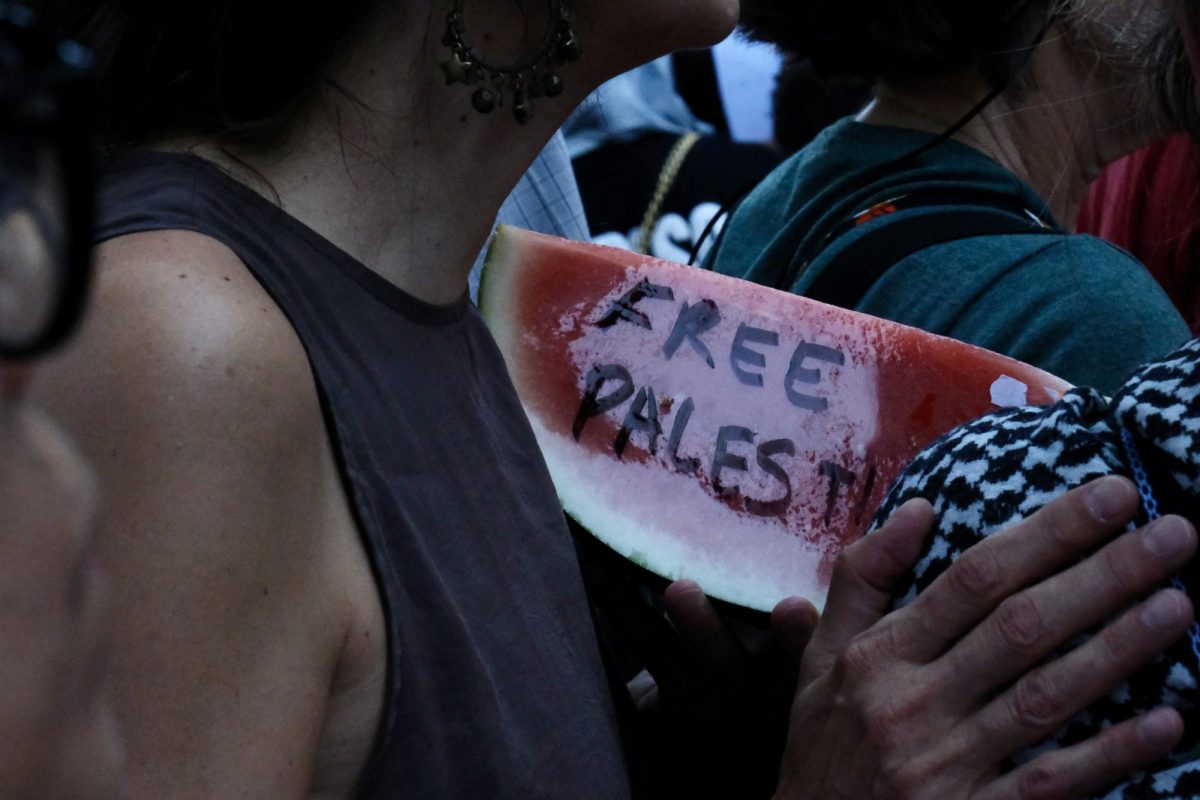 Pro-Palestine protester carries a fresh watermelon slice while chanting hymns with both the crowd and the band.